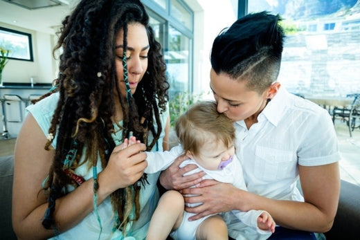 Two mothers holding their baby on the couch