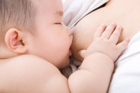 Close-up of a baby breastfeeding, with eyes closed and one hand resting on the parent's chest.