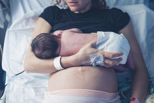 New mother in a hospital bed breastfeeding her newborn baby, with a visible postpartum belly, hospital bracelet, and IV, often associated with recovery after a C-section