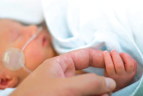 Premature baby holding onto and adult index finger