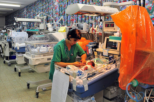 Image of a nurse tending to a newborn baby in a NICU incubator