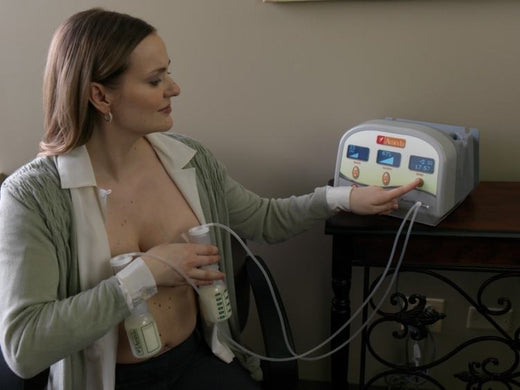 Mother using an Ameda double electric breast pump, holding two milk collection bottles while adjusting the settings on the Ameda pump device.