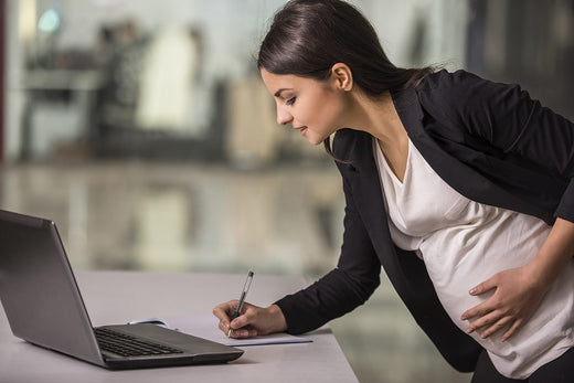 Pregnant mother writing on a notepad next to her open laptop at work