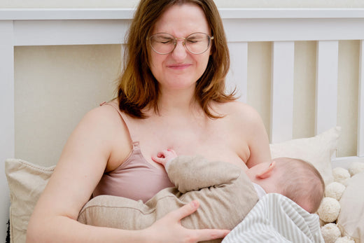 Woman wincing while breastfeeding her baby in bed