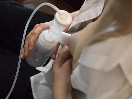 Close-up of a person using a breast pump, holding the flange and milk collection bottle against their chest.