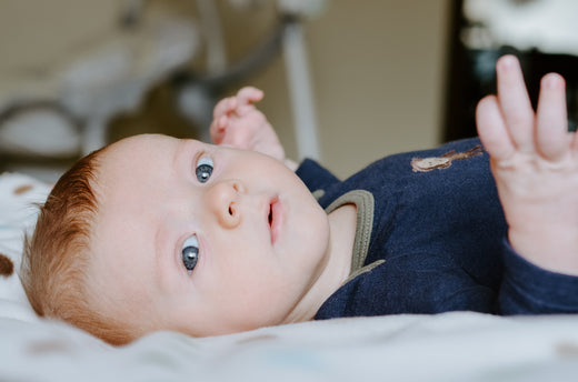 Baby with red hair lying on their back, looking up with wide eyes, wearing a navy blue onesie.