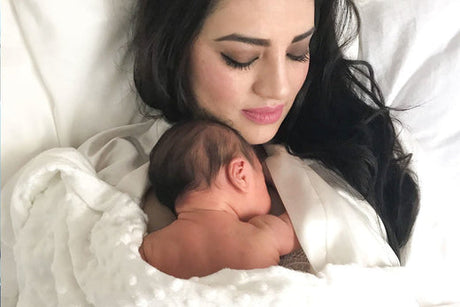 Mother holding her sleeping newborn baby on her chest in bed