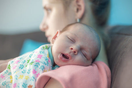 Newborn baby sleeping on the shoulder of a mother looking stressed or tired.