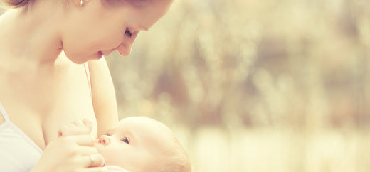 Mother breastfeeding her baby while looking down lovingly, with a soft, natural background.