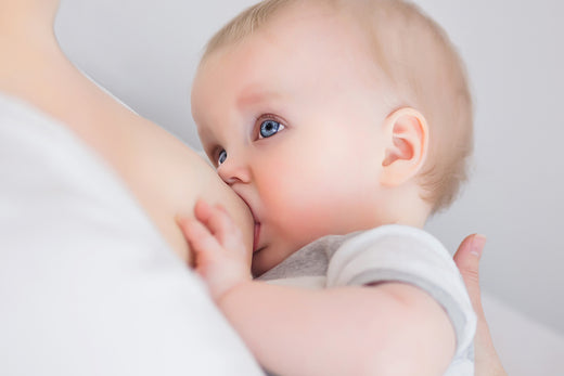 Close-up of a baby breastfeeding, with blue eyes gazing upward while nursing.