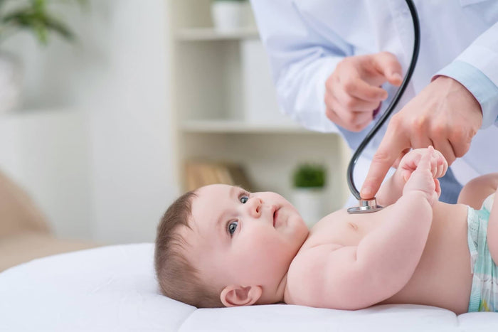 Doctor using a stethoscope to check the heartbeat of a baby lying on an examination table.