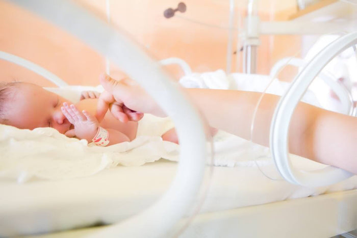 Close-up of a mother holding the flanges of an Ameda breast pump against her chest while expressing milk.