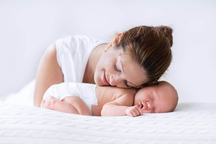 Mother smiling while using an Ameda breast pump, holding the flanges against her chest in a comfortable seated position.