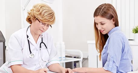 Doctor with a stethoscope consulting a female patient, both seated at a desk in a medical office.