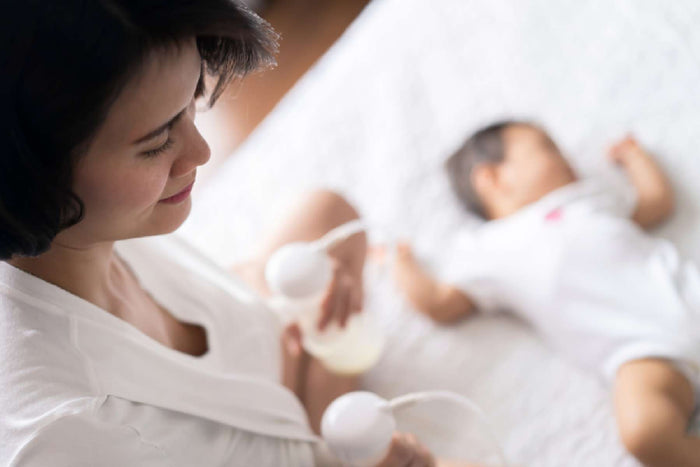 Mother sitting and using an Ameda breast pump, with a close-up view of the flanges held against her chest during milk expression.