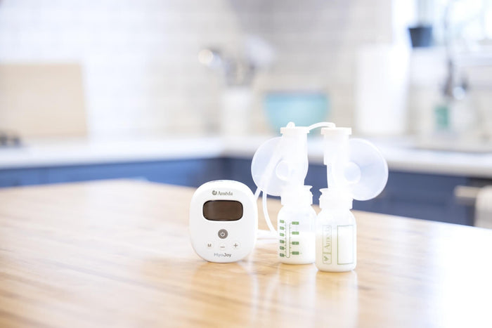 Ameda Mya Joy breast pump, including pump unit, flanges, and two milk collection bottles with milk, displayed on a wooden kitchen countertop.