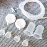 A collection of clear and white medical or therapeutic components arranged on a gray textured surface. There are two larger white caps with pull-out tubes, two frosted cylindrical cups, and several smaller clear suction cups. A flexible transparent tube is coiled among the components, forming a gentle loop. The arrangement is neat and organized, providing a sense of functionality and purpose.