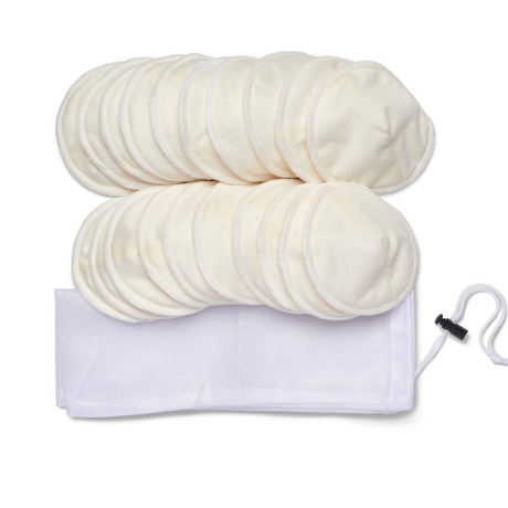 A collection of round, soft, cream-colored cotton pads stacked in two piles. There are a total of 16 pads visible, neatly arranged in a way that shows their circular shape and texture. Next to the pads is a white mesh laundry bag with a drawstring closure, positioned horizontally. The overall composition emphasizes the pads as a reusable product, ideal for personal care or cosmetic use.