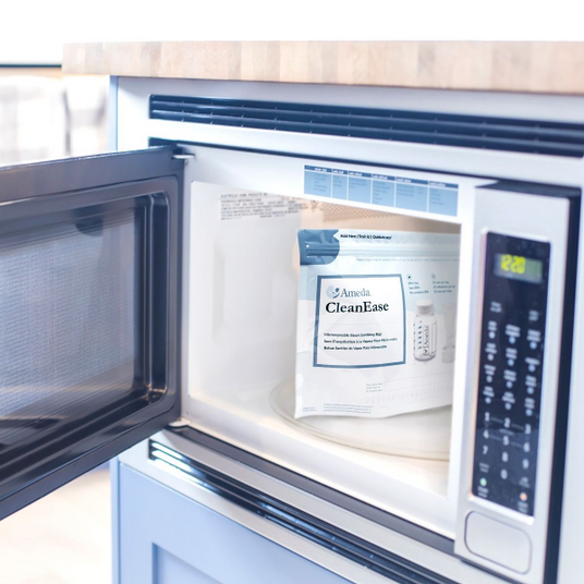 A modern microwave with an open door, revealing a package labeled "Ameda CleanEase" sitting on a circular glass turntable inside. The package is predominantly white with light blue accents, and it appears to contain cleaning supplies for breastfeeding equipment. The microwave’s control panel with buttons and a digital display showing the time is visible on the right side. The background is softly blurred, indicating a bright and spacious kitchen environment.